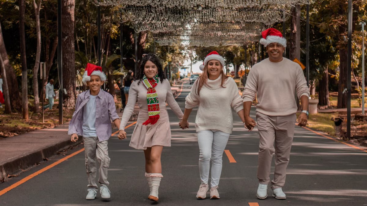A joyful family walks down a decorated street wearing Christmas hats, symbolizing holiday spirit.